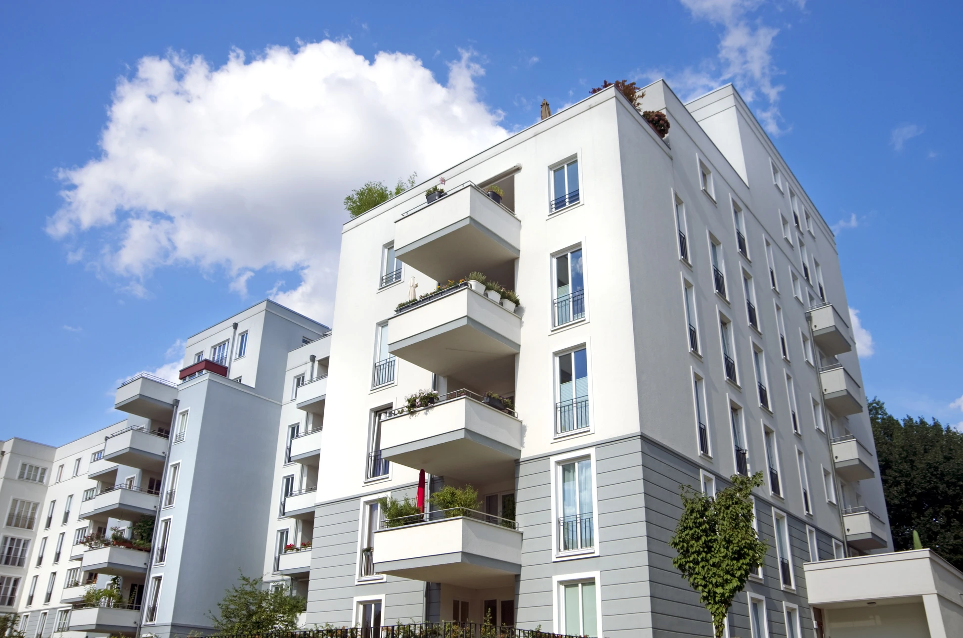 Façade d'immeubles résidentiels modernes avec balcons et terrasses végétalisées sous ciel bleu nuageux